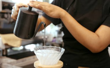 Önlük takan bir kadın kafe işletmecisi müşterilere kahve hazırlamak için kavrulmuş kahve telvesine sıcak su döker..