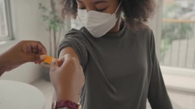 Bir kadın doktor aşılandıktan sonra çocuğun omzuna alçı uyguluyor. Çocuklar yüz maskesi takarlar. Grip ya da salgın hastalığa karşı aşı kolları açmak ve aşı kavramı.