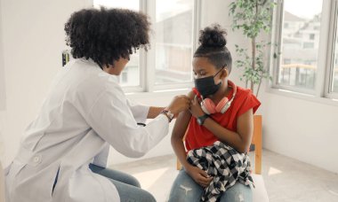 Afrikalı Amerikalı doktor, aşılandıktan sonra çocuğun omzuna alçı uyguluyor. Grip ya da salgın hastalığa karşı aşı kolları açmak ve aşı kavramı.