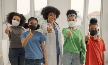 Afro-Amerikalı doktor ve maskeli çocuklar hastanede ya da klinikte mutlu parmaklar.