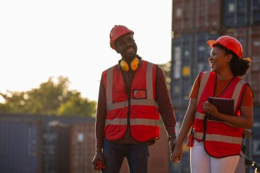 Endüstriyel konteynır deposunda güven ve başarıyla gülümseyen iki Afrikalı erkek ve kadın işçi..