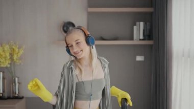 Genç kız elektrik süpürgesiyle yerleri temizlerken eğleniyor. Evde ev işi yapan mutlu kadın kulaklık takan müziğin tadını çıkarıyor..