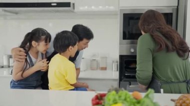 Mutlu aile, anne, baba ve çocuklar birlikte yemek pişiriyor, ebeveynler çocuklara öğretiyor kız evlat taze sebze salatası ve kruvasan pişiriyor modern mutfakta birlikte sağlıklı yiyecekler hazırlıyorlar.