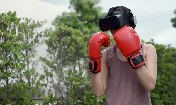 Young female wearing VR headset for working out boxing, aerobic training for boxing punch in virtual reality in simulation world.
