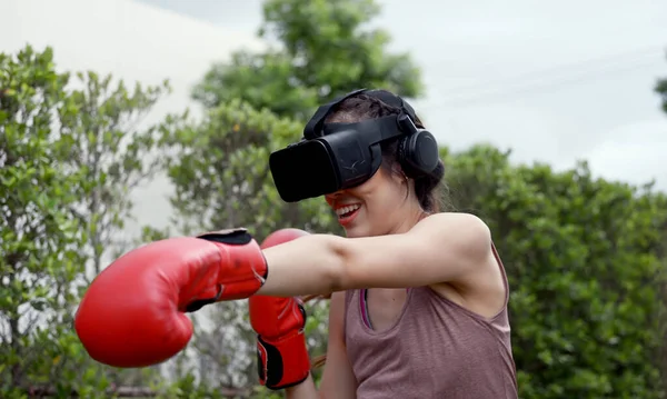 Young female wearing VR headset for working out boxing, aerobic training for boxing punch in virtual reality in simulation world.