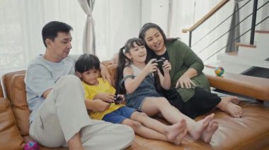Sevimli çocuklu mutlu aile bireyleri kanepede oturup video oyunu oynuyorlar..