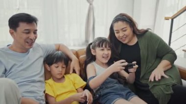 Sevimli çocuklu mutlu aile bireyleri kanepede oturup video oyunu oynuyorlar..