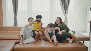 Sevimli çocuklu mutlu aile bireyleri kanepede oturup video oyunu oynuyorlar..