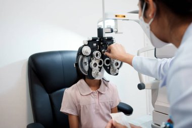 Klinikte Asyalı bir kızın gözlerini inceleyen bir oftalmolog. Koruyucu yüz maskeleri takıyorlar..
