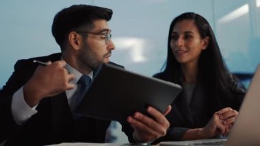 İki meslektaş, bilgisayar ya da not defteri kullanarak pazarlamayı analiz eden verileri tartışıyor iş arkadaşlarıyla ofis masasında oturmalarına yardımcı oluyorlar..