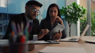 İki meslektaş, bilgisayar ya da not defteri kullanarak pazarlamayı analiz eden verileri tartışıyor iş arkadaşlarıyla ofis masasında oturmalarına yardımcı oluyorlar..