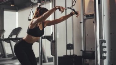 Sporty woman exercising on multistation at gym for arm and shoulders muscles. Fitness exercising in gym.