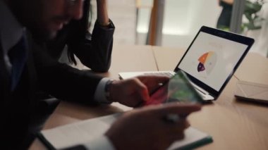 İki meslektaş, bilgisayar ya da not defteri kullanarak pazarlamayı analiz eden verileri tartışıyor iş arkadaşlarıyla ofis masasında oturmalarına yardımcı oluyorlar..