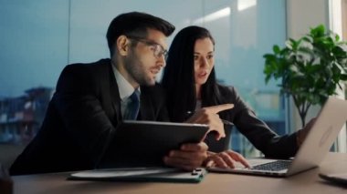 İki meslektaş, bilgisayar ya da not defteri kullanarak pazarlamayı analiz eden verileri tartışıyor iş arkadaşlarıyla ofis masasında oturmalarına yardımcı oluyorlar..