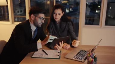 İki meslektaş, bilgisayar ya da not defteri kullanarak pazarlamayı analiz eden verileri tartışıyor iş arkadaşlarıyla ofis masasında oturmalarına yardımcı oluyorlar..