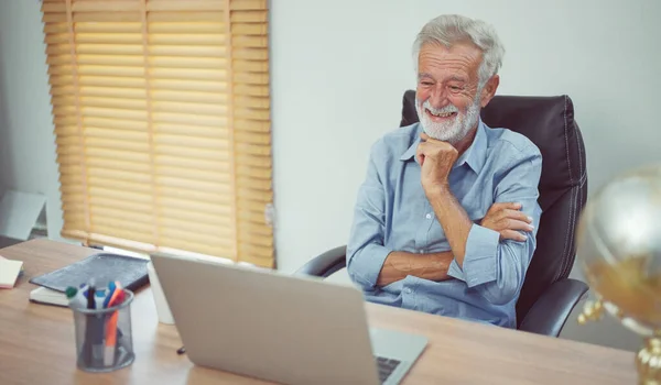Happy senior older man using laptop computer at work desk.