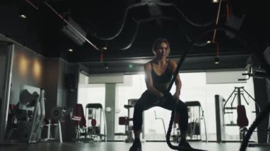 Active dedicated motivated female athlete training in gym with battle ropes, achieving goals enjoying healthy lifestyle.