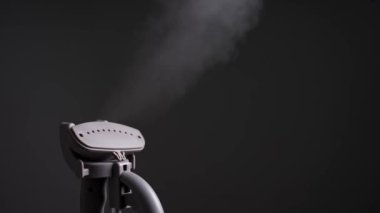 Close up of electric hand steam generator while it's hot and steam comes out on the ironing board place for clothes on black background.Home equipment for housework concept .