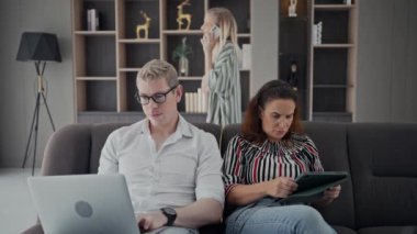 Gadgets addiction. Young caucasian of three holding and using different electronic devices while sitting on sofa in living room at home . Parents and their daughter with modern gadgets