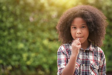 Happy African-American kid girl with a lollipop in her hands in the garden or outdoors.