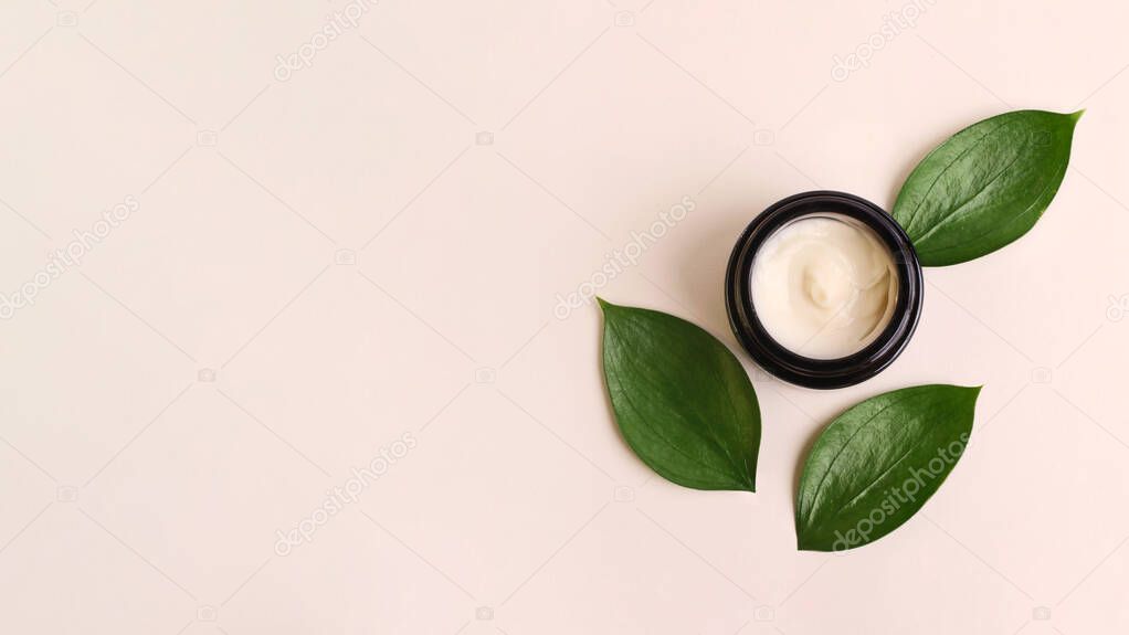 Round cosmetic cream container on the beige background,fresh juicy green leafs around.Organic cosmetics concept.Flat lay,large banner.