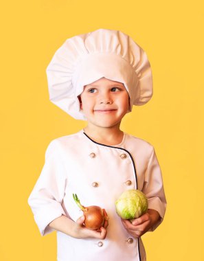 Beyaz şef üniformalı komik çocuk elinde lahana ve soğan tutuyordu. Neşeli sarı arka plan.