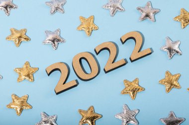 Mavi arkaplanda 2022 ahşap numaraların üst görüntüsü. Altın ve gümüş yıldızlar. Şenlikli bir konsept..
