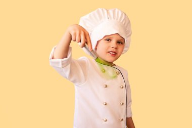 Elinde çırpıcıyla beyaz şef üniforması içinde gülümseyen bir çocuk. Neşeli sarı arka plan.