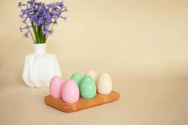 Pastel Easter eggs in the wooden tray.Violet flowers on background. — Stock Photo, Image