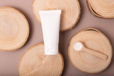 Tahta dilimlerdeki boş kozmetik tüpünün üst görüntüsü. Yanında kolajen olan kaşık. Dünya tonları, çevre dostu kavram..