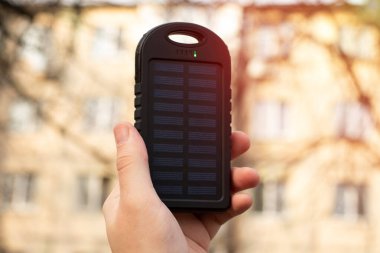 İnsan elinin yakın plan fotoğrafı, güneş pili ve şarj cep telefonu ile enerji bankasını tutuyor..