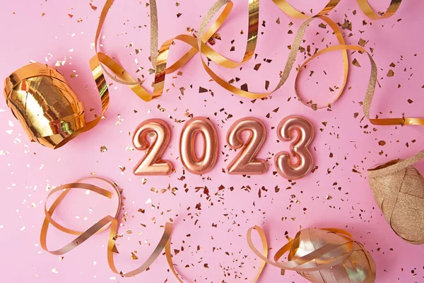 Top view of rose gold numbers 2023 with gold confetti and glitter on pink background.Festive banner,flat lay style.