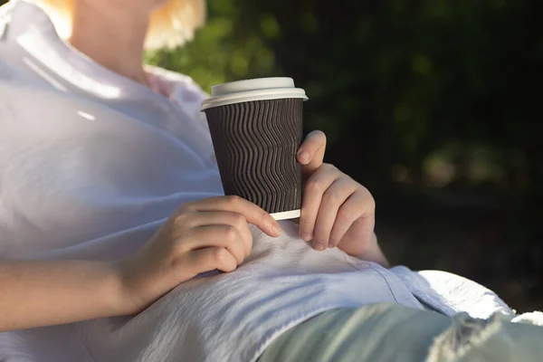 Anonymous woman holding craft paper cup with coffee outside.