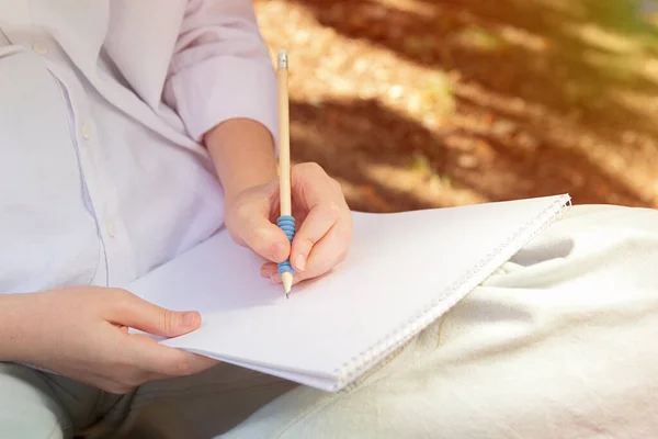 Anonymous girl making notes in the blank paper album,sunlight on background.