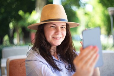 Smiling millennial woman in hat making selfie outside.