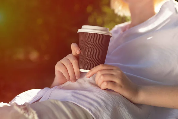 Anonymous woman holding craft paper cup with coffee outside,sunlight on background.