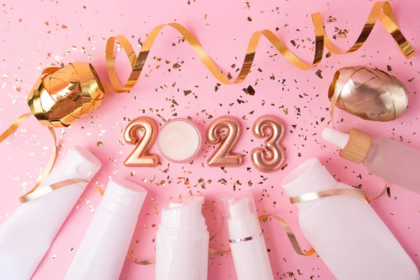 Top view of the cosmetics containers on pink background.Rose gold numbers 2023 above.Good for new year offer and text overlay.