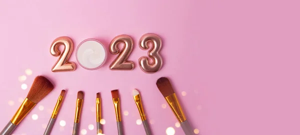 Top view of the makeup brushes on pink background.Rose gold numbers 2023 above.Good for new year offer and text overlay,large banner with copy space.
