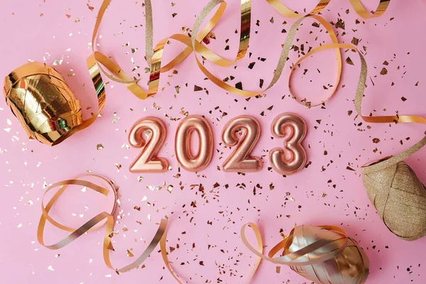 Top view of the cosmetics containers on pink background.Rose gold numbers 2023 above and golden confetti.