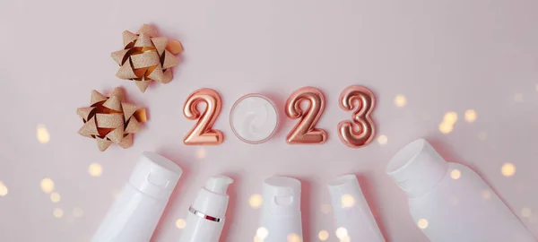 Gri arka plandaki kozmetik konteynırlarının üst görüntüsü. Yukardaki gül altın rakamları 2023. Yeni yıl teklifi ve metin örtüsü için iyi.
