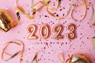 Top view of the cosmetics containers on pink background.Rose gold numbers 2023 above and golden confetti.