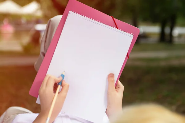 Anonymous girl making notes or drawing in the blank paper book,sunlight on background.