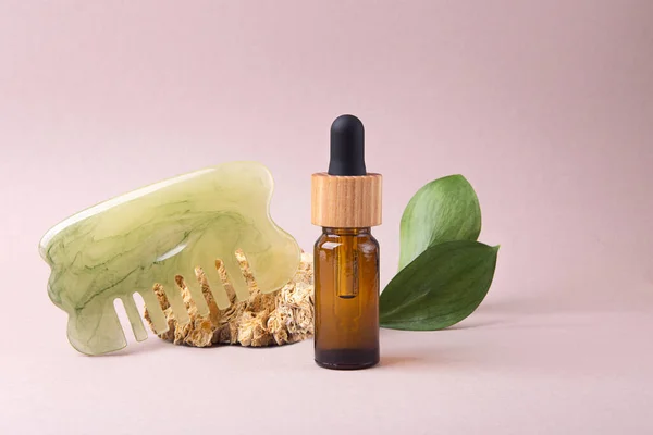 Eco friendly cosmetics oil dropper with hair brush near it,green leafs on background.Concept of hair care.