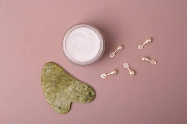 Top view of open cosmetics container with cream,cosmetics capsules and guasha near it.