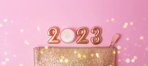 Top view of rose gold numbers 2023 and face cream from above,golden cosmetic bag near it.Good for new year offer and text overlay.