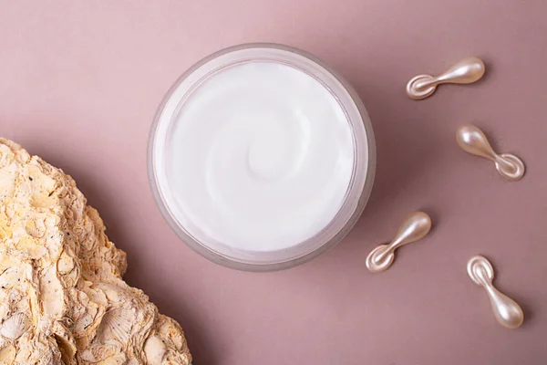 Top view of open cosmetics container with cream,cosmetics capsules and natural stone near it.