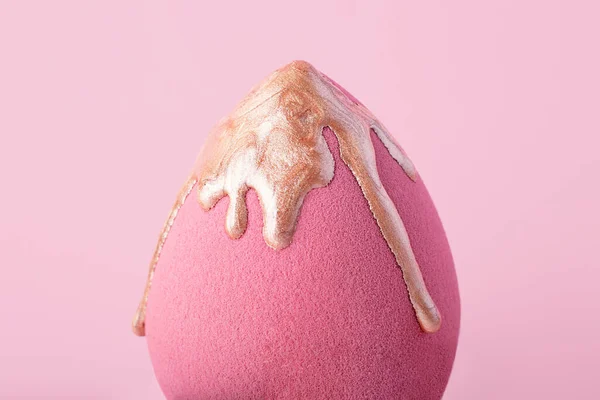 Closeup photography of beauty blender with dripping bronzer on it.Neutral pink background.