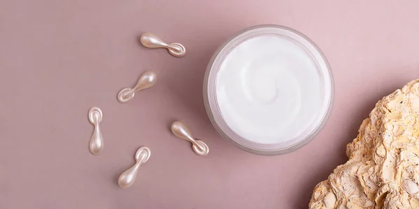 Top view of open cosmetics container with cream,cosmetics capsules and natural stone near it.Large banner with negative space.