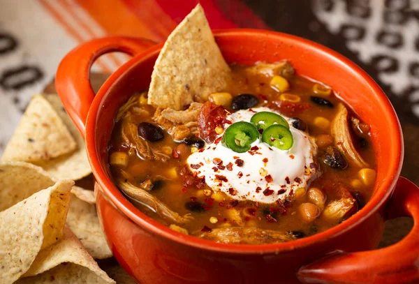 Close-up of a bowl of chicken taco soup topped with sour cream and serrano peppers with tortilla chips
