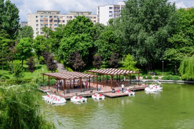 Bükreş, Romanya - 29 Mayıs 2021: Romanya 'nın Bükreş kentindeki Moghioros Parkı olarak da bilinen Drumul Taberei Parkı' ndaki göl ve canlı yeşil ağaçlarla manzara bulutlu bir yaz gününde